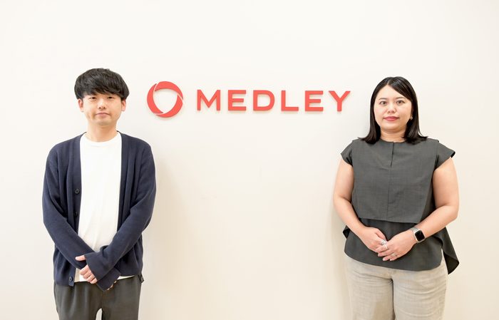 株式会社メドレーAI推進室の澤渡美沙子様と伊藤優樹様がMEDLEYロゴの前で並んで立っている写真です