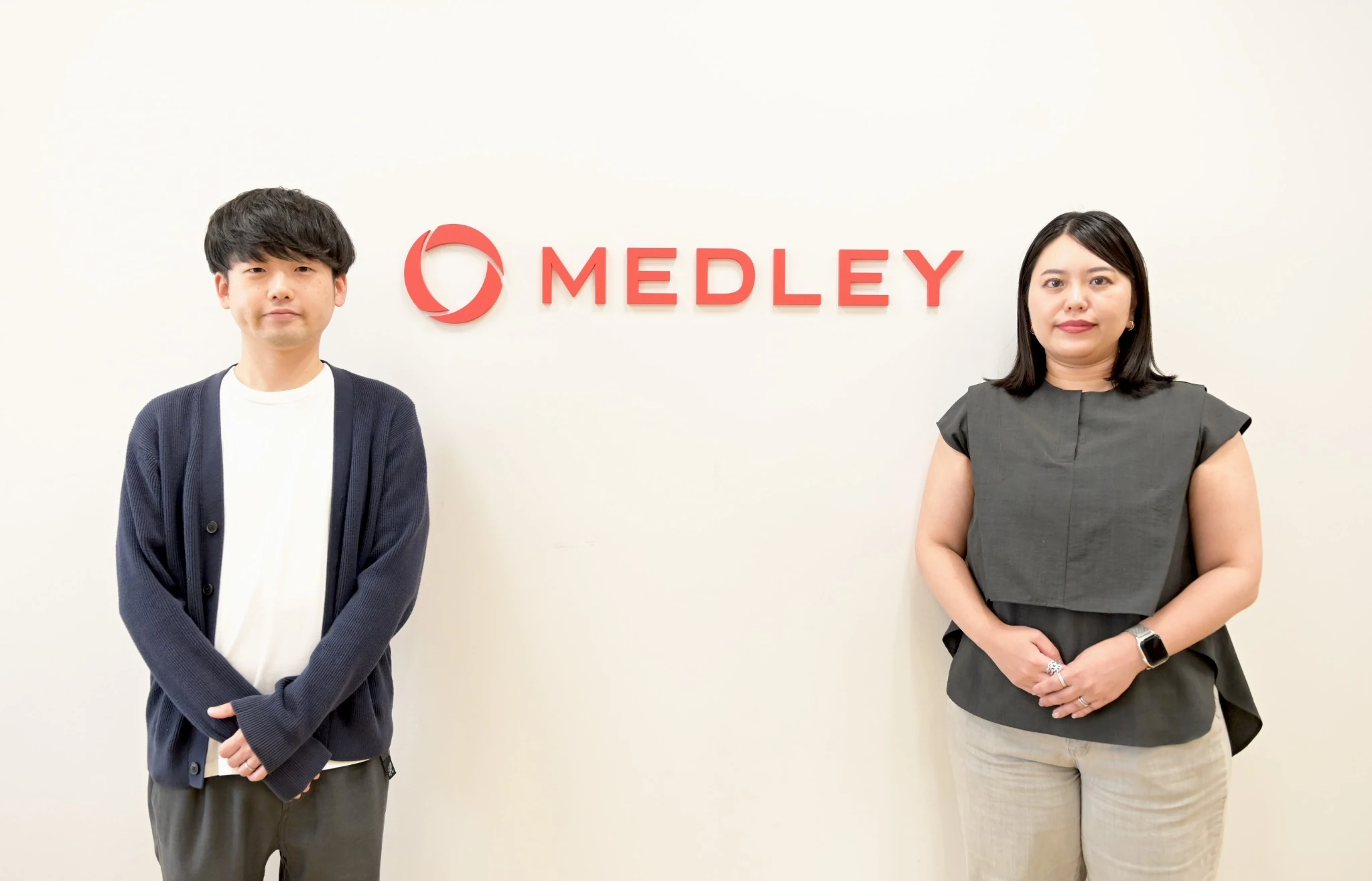 株式会社メドレーAI推進室の澤渡美沙子様と伊藤優樹様がMEDLEYロゴの前で並んで立っている写真